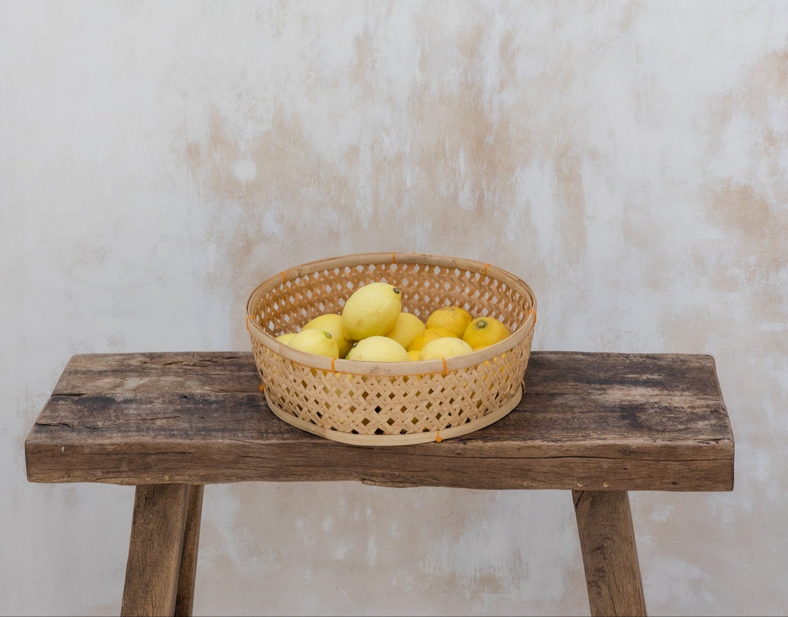 Woven basket of lemons resting on a rustic stool against a stone wall—symbolizing warmth, simplicity, and approachable connection.