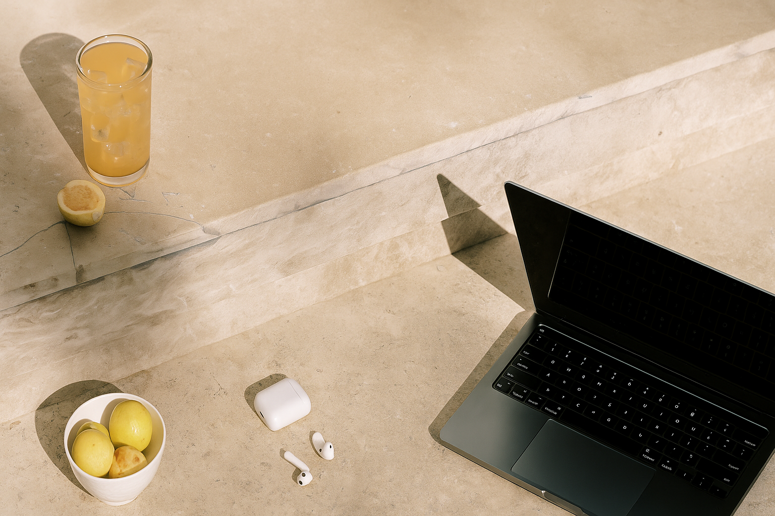 Minimalist concrete workspace with a laptop, fresh lemon water, and earphones—capturing intentional, balanced business-building vibes.