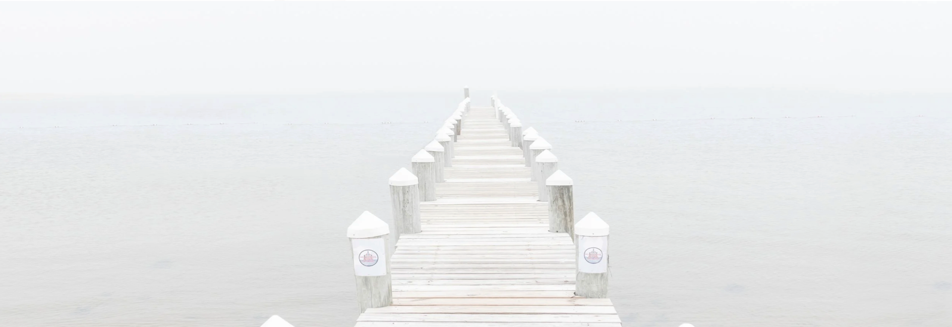 White wooden pier extending into the fog with light posts on a white background